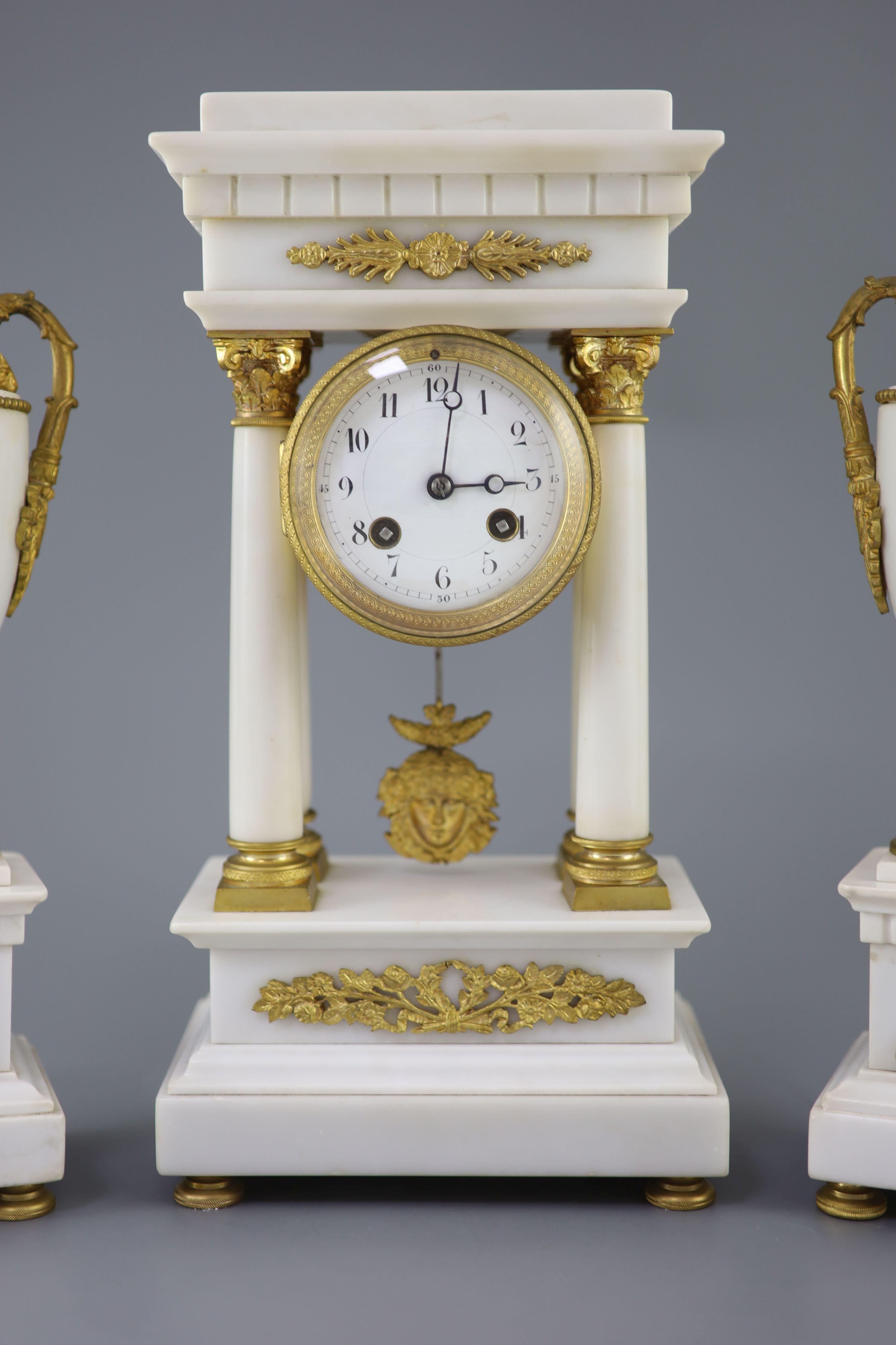 A Louis XVI style ormolu mounted white marble clock garniture, clock 14.5in. urns 13.75in.